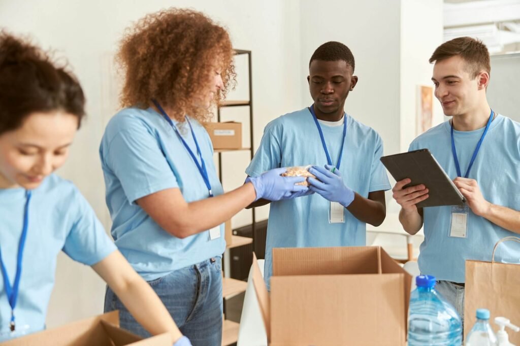 Diverse Young Volunteers In Protective Gloves Sorting Packing Foodstuff In Cardboard Boxes Working 1024x682